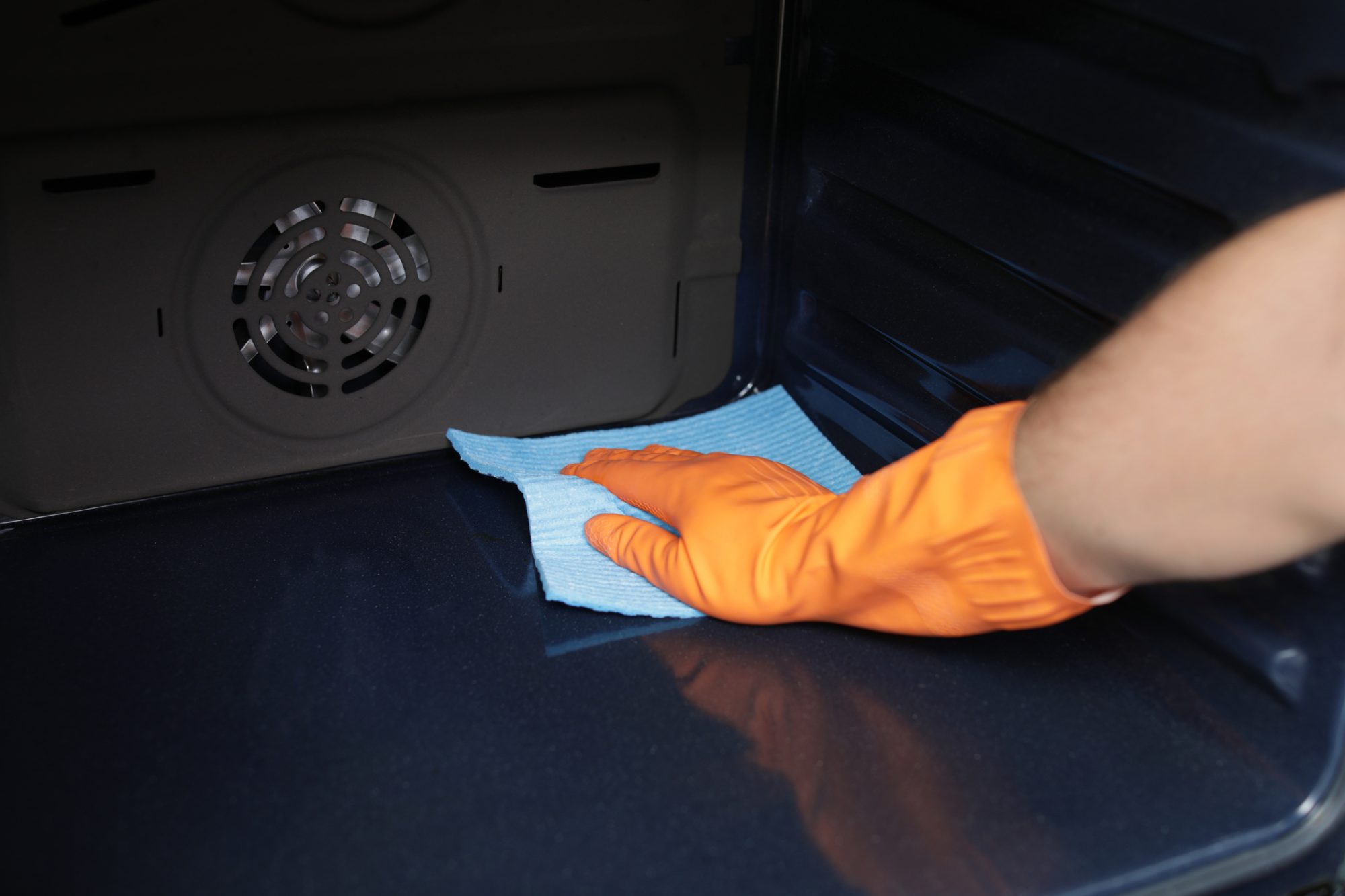 Young man cleaning oven with rag in kitchen, closeup